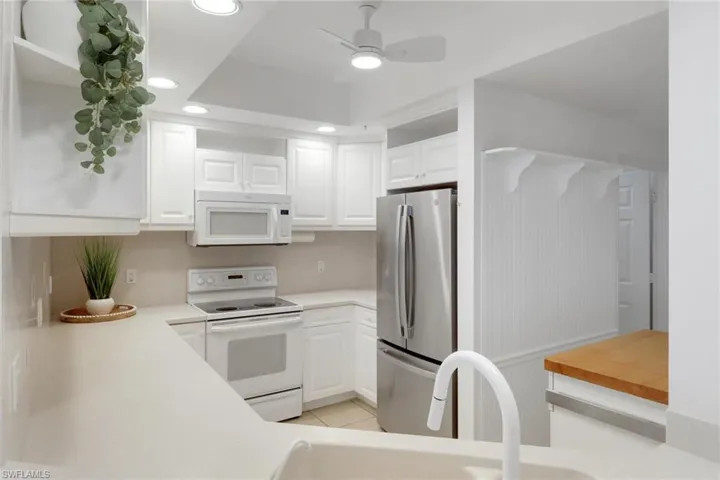 Kitchen featuring white cabinetry with underside lighting, sink, white appliances, new ceiling fan, and light tile patterned flooring