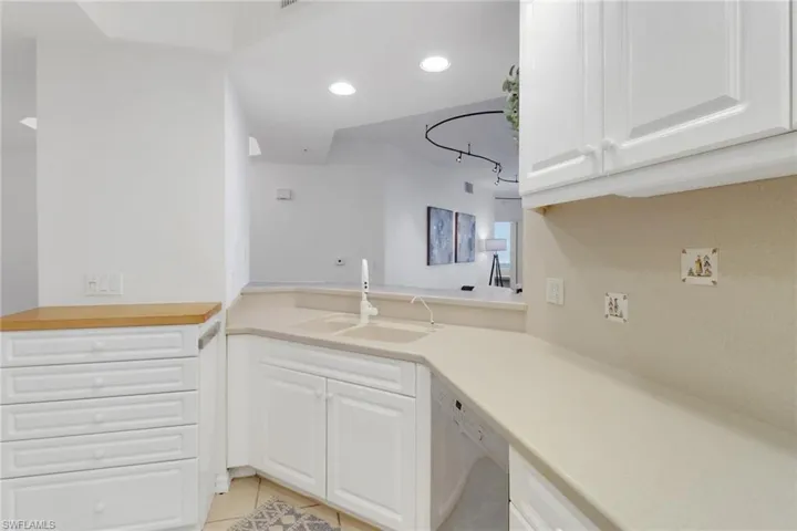 Kitchen with sink, additional storage with butcher block counter, corian counter tops, light tile patterned floors, white cabinetry with underside lighting, and dishwasher