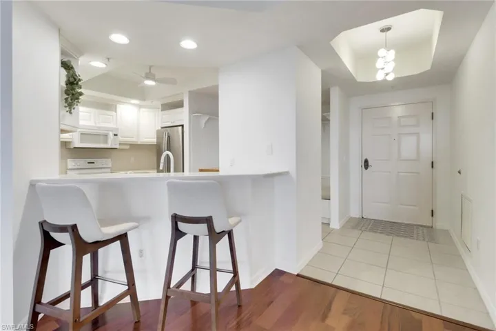 Kitchen with white cabinetry, breakfast bar, wood flooring, new hanging light fixtures, and stainless steel refrigerator