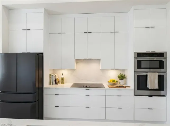 Kitchen with black appliances, modern cabinets, white cabinets, and light stone counters