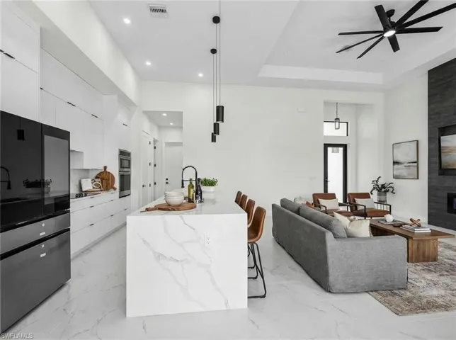 Kitchen with modern cabinets, stainless steel appliances, a kitchen breakfast bar, white cabinetry, and light stone countertops