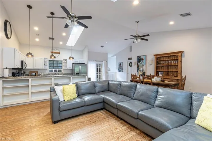 Living room with a skylight, ceiling fan, light wood finished floors, high vaulted ceiling, and recessed lighting