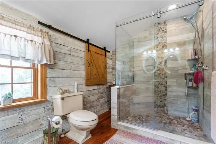 Bathroom with vaulted ceiling, a shower stall, toilet, and wood finished floors
