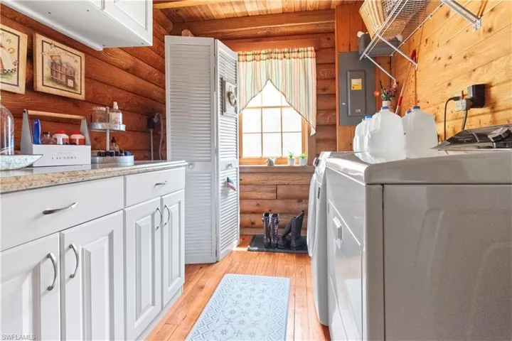 Laundry room featuring rustic walls, washer / dryer, light wood-style floors, electric panel, and cabinet space
