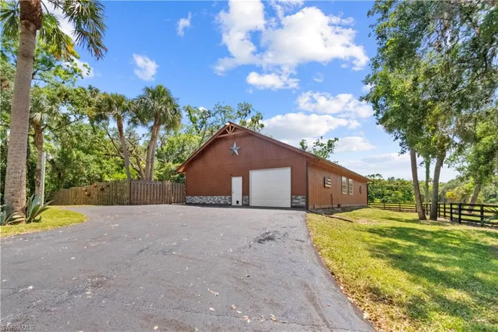 View of property exterior featuring fence, a lawn, driveway, and a garage