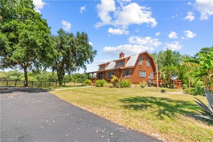 View of front of home with fence, a gambrel roof, log siding, and a front yard