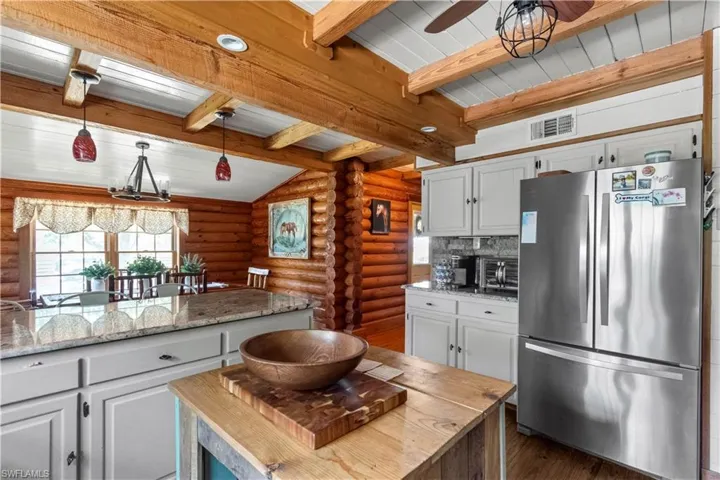 Kitchen featuring rustic walls, visible vents, beam ceiling, dark wood-style floors, and freestanding refrigerator