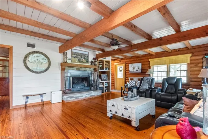 Living room featuring a ceiling fan, a stone fireplace, visible vents, and hardwood / wood-style floors