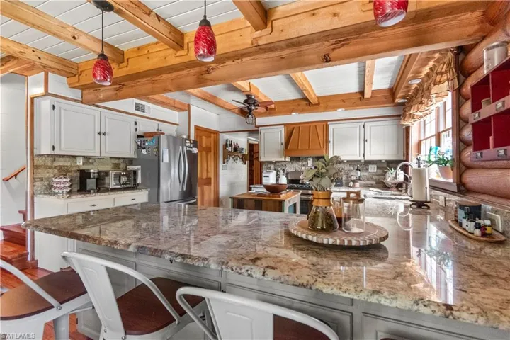Kitchen with tasteful backsplash, a sink, a kitchen bar, beam ceiling, and freestanding refrigerator