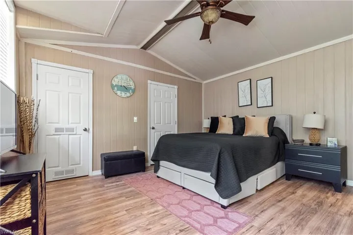Bedroom with lofted ceiling, wooden walls, visible vents, light wood-style floors, and ceiling fan