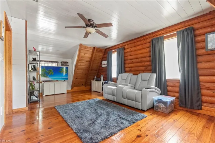 Living area featuring log walls, light wood-style flooring, wooden ceiling, and ceiling fan