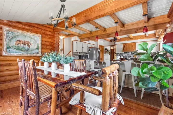 Dining room featuring rustic walls, a chandelier, beamed ceiling, light wood-style flooring, and wooden ceiling