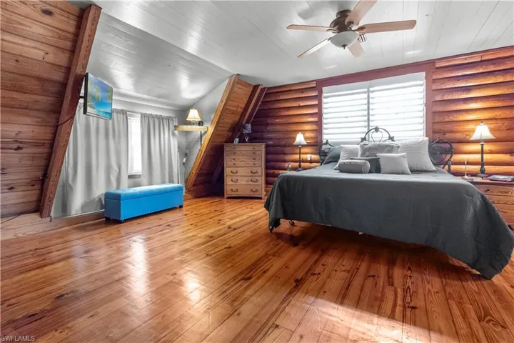 Bedroom featuring a ceiling fan, rustic walls, and wood-type flooring