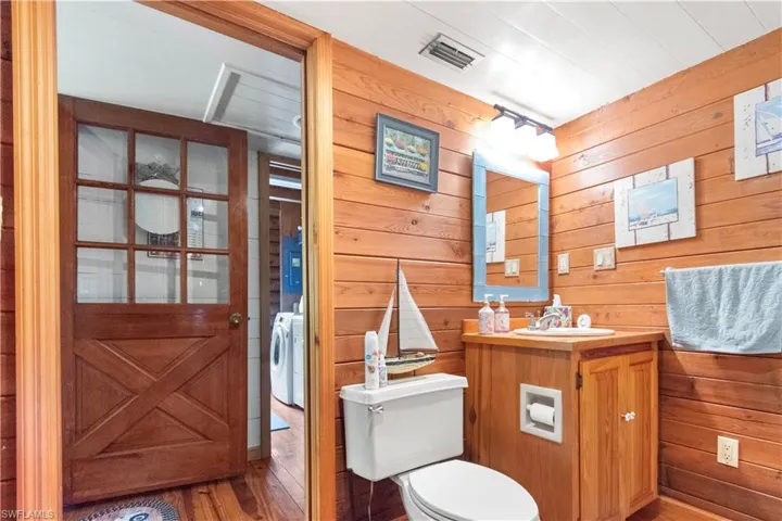 Half bathroom with wood walls, toilet, wood finished floors, and washer / dryer