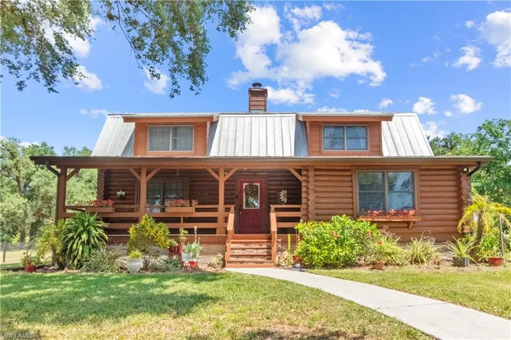 Log-style house with a front lawn, covered porch, log exterior, and metal roof