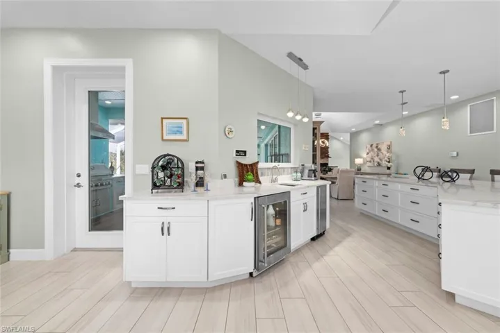 Kitchen with beverage cooler, wet bar, white cabinetry and decorative light fixtures