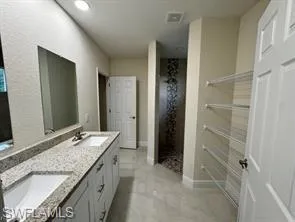 Dual-sink vanity with stone countertop, tile flooring, and walk-in shower with decorative vertical tile inlay and built-in wire shelving