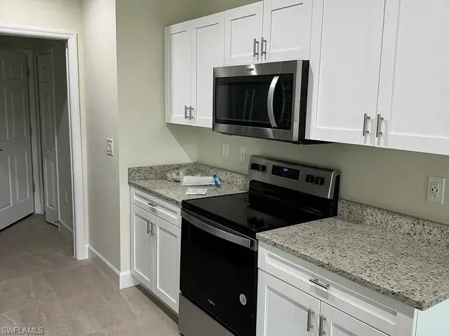White shaker-style cabinetry, stone-finish countertops, stainless steel microwave, black electric range, and tiled flooring