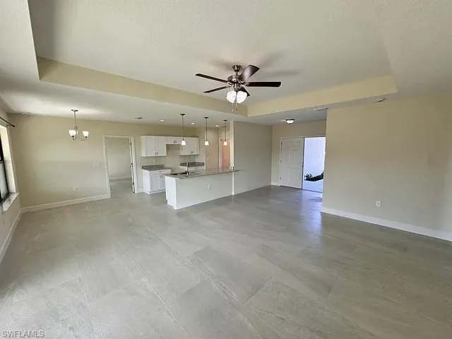 Tray ceiling, neutral tile flooring, kitchen with white cabinetry, stone-surface countertops, and recessed lighting