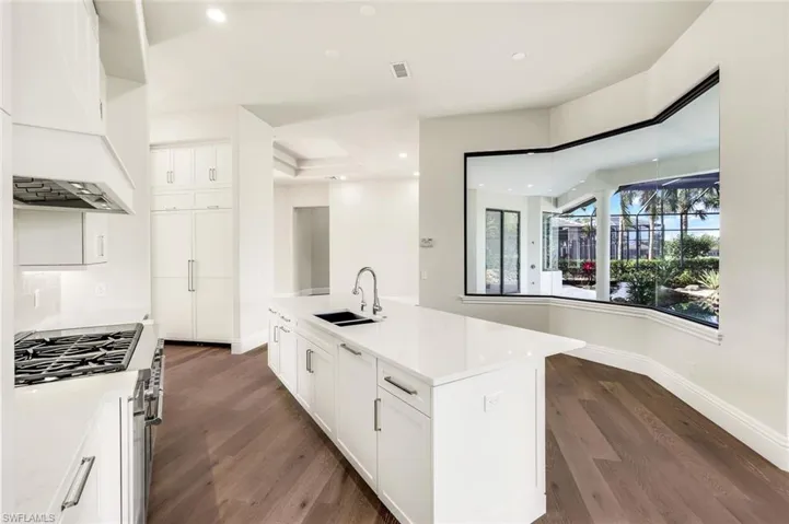 Kitchen with premium range hood, stainless steel gas cooktop, sink, a center island with sink, and white cabinets
