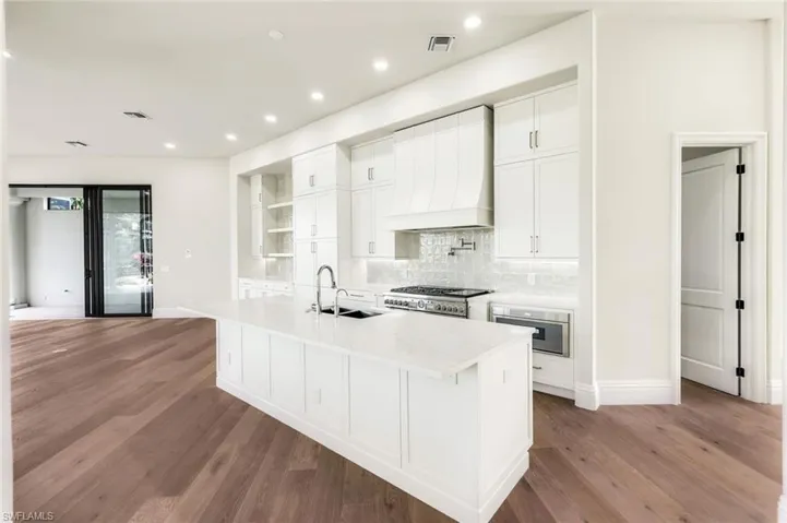 Kitchen featuring sink, premium range hood, light hardwood / wood-style floors, an island with sink, and white cabinets