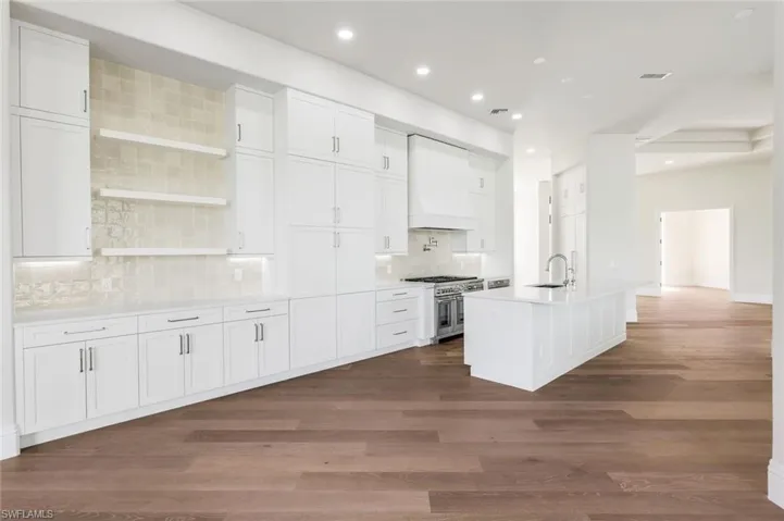 Kitchen with custom exhaust hood, sink, range with two ovens, and white cabinets