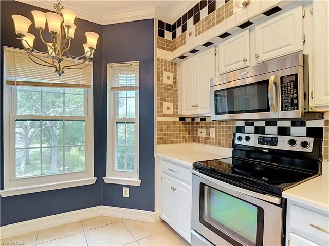 Kitchen featuring white cabinetry, stainless steel appliances, decorative mosaic tile backsplash, multi-light chandelier, and large windows