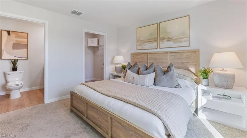 Model home. Bedroom featuring light colored carpet, a walk in closet, and connected bathroom
