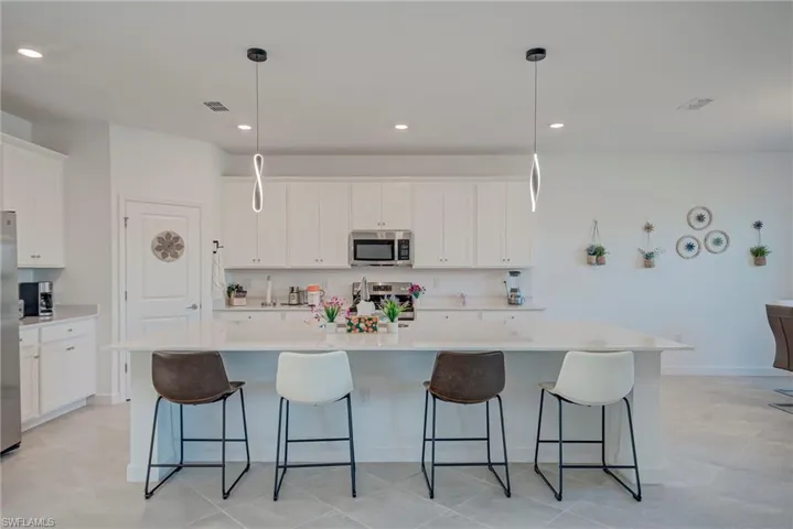 Kitchen with an island with sink, decorative light fixtures, white cabinets, a kitchen bar, and recessed lighting