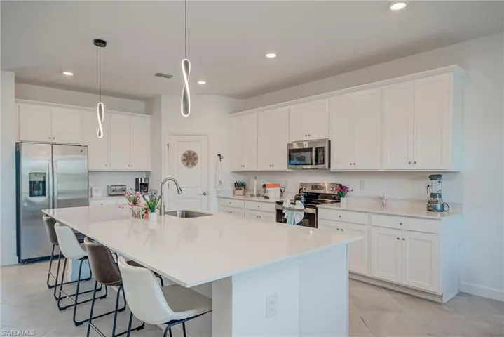 Kitchen with white cabinetry, appliances with stainless steel finishes, a breakfast bar area, a large island with sink, and recessed lighting