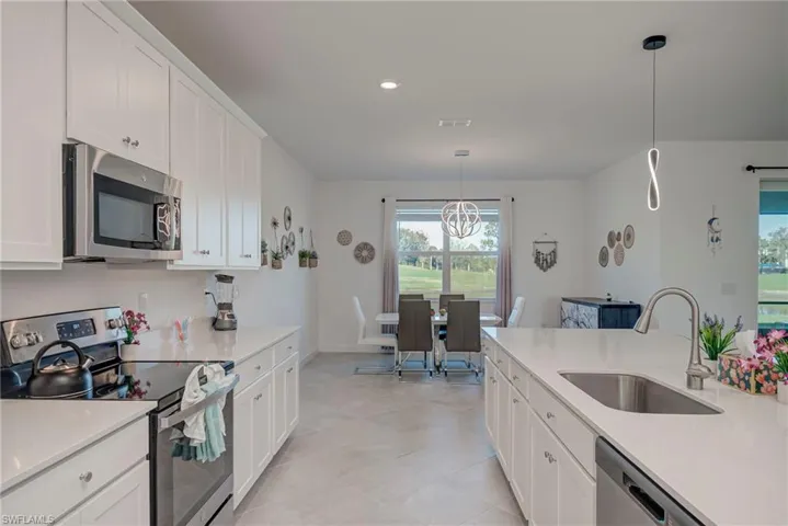 Kitchen with appliances with stainless steel finishes, white cabinets, decorative light fixtures, light stone counters, and recessed lighting