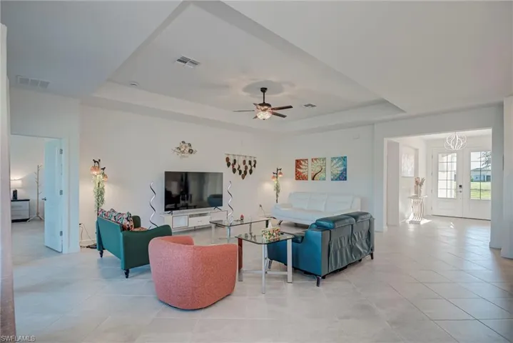 Living room featuring a tray ceiling, ceiling fan, and light tile patterned floors