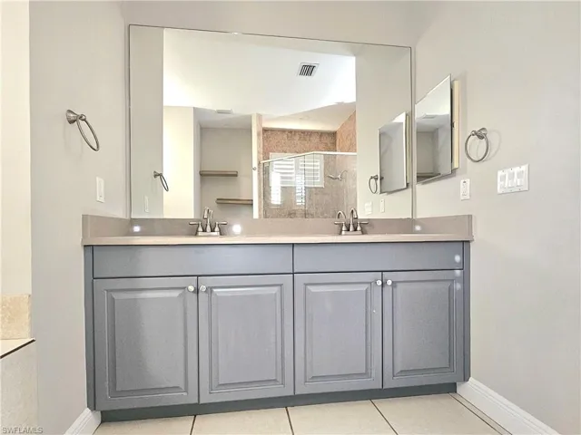 Full bathroom with a shower stall, baseboards, double vanity, and tile patterned flooring