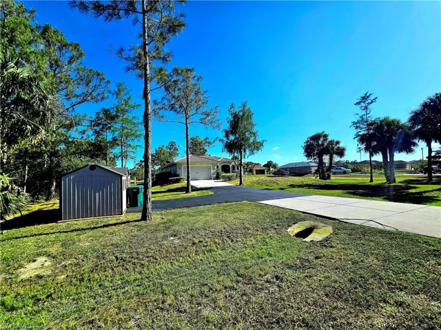View of green lawn with driveway, a storage unit, a garage, and an outdoor structure