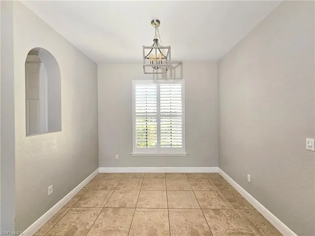 Spare room featuring a chandelier, baseboards, light tile patterned flooring, and arched walkways
