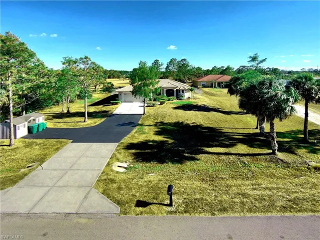 View of property hidden behind natural elements with driveway, a front yard, and a garage