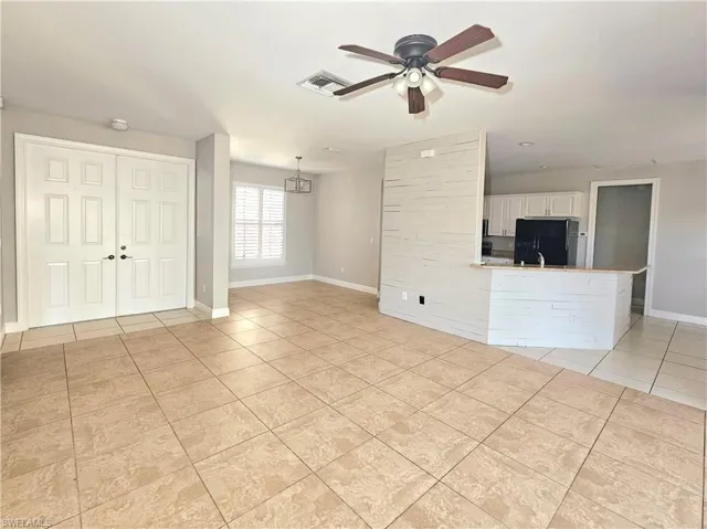 Unfurnished living room featuring light tile patterned flooring, a ceiling fan, and baseboards