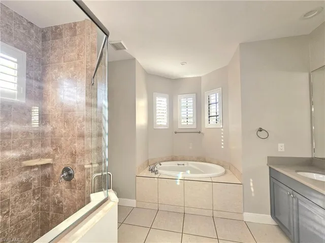 Full bathroom featuring a shower stall, tile patterned flooring, a garden tub, baseboards, and vanity