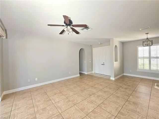 Unfurnished room with arched walkways, ceiling fan, light tile patterned floors, and baseboards