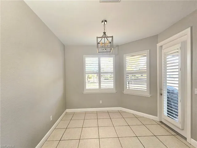 Unfurnished dining area with a chandelier, healthy amount of natural light, light tile patterned flooring, and baseboards