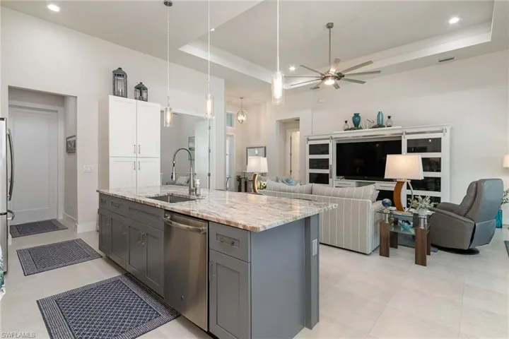 Kitchen featuring dishwasher, granite counters, a kitchen island with sink, and gray cabinetry
