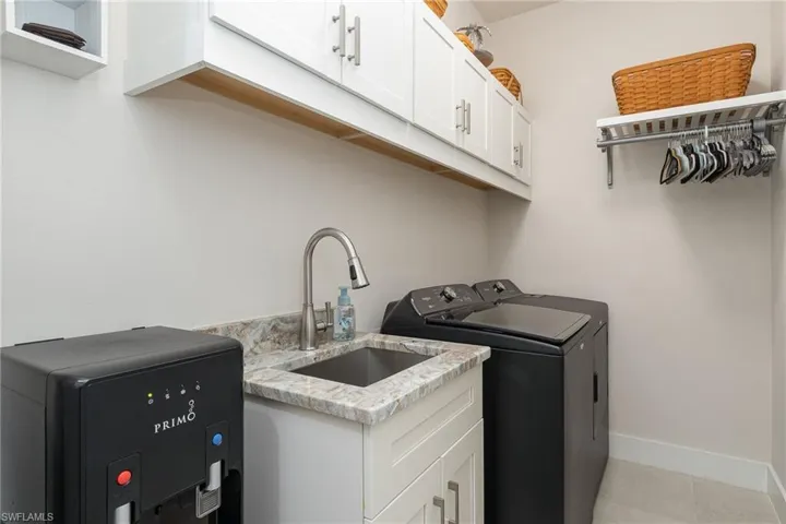 Laundry room featuring washing machine and dryer, sink, light tile patterned floors, and cabinets