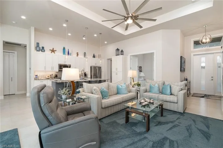 Tiled living room featuring ceiling fan, a raised ceiling, and a high ceiling