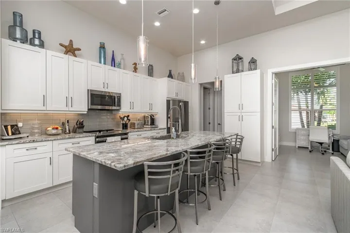 Kitchen with light stone counters, a breakfast bar area, white cabinetry, stainless steel appliances, and a center island with sink