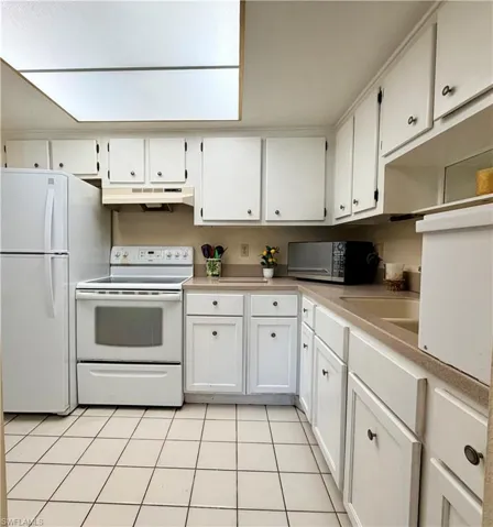 Kitchen featuring electric range, light countertops, microwave, white cabinetry, large pantry and light tile flooring