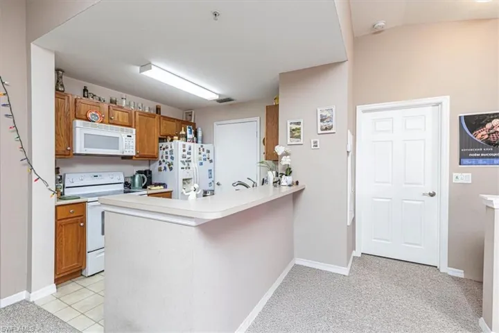 Kitchen featuring brown cabinetry, white appliances, light countertops, a peninsula, and light colored carpet