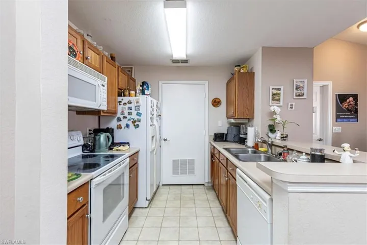 Kitchen featuring white appliances, a peninsula, brown cabinetry, and light countertops