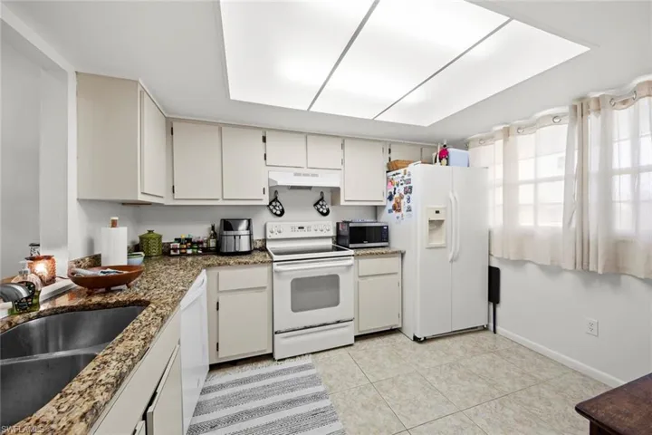Kitchen with white appliances, sink, light tile patterned floors, dark stone countertops, and white cabinets