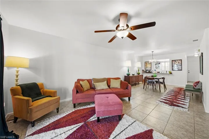 Tiled living room with ceiling fan with notable chandelier