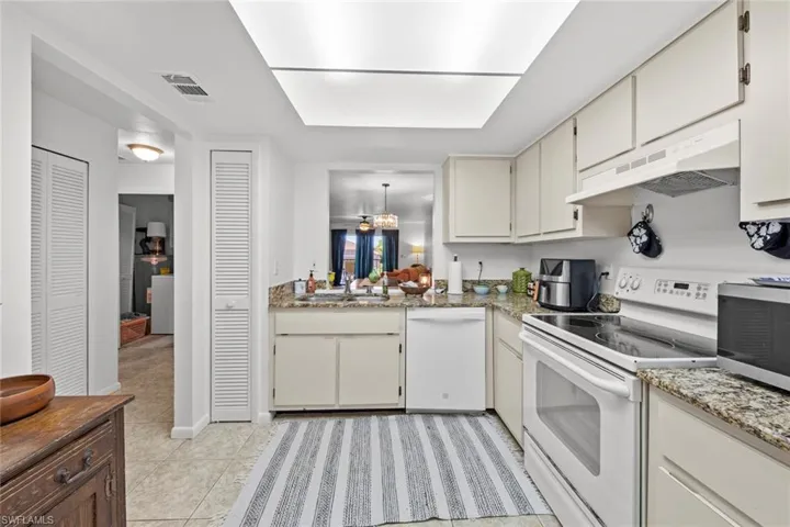 Kitchen with white appliances, ventilation hood, sink, a skylight, and light tile patterned flooring